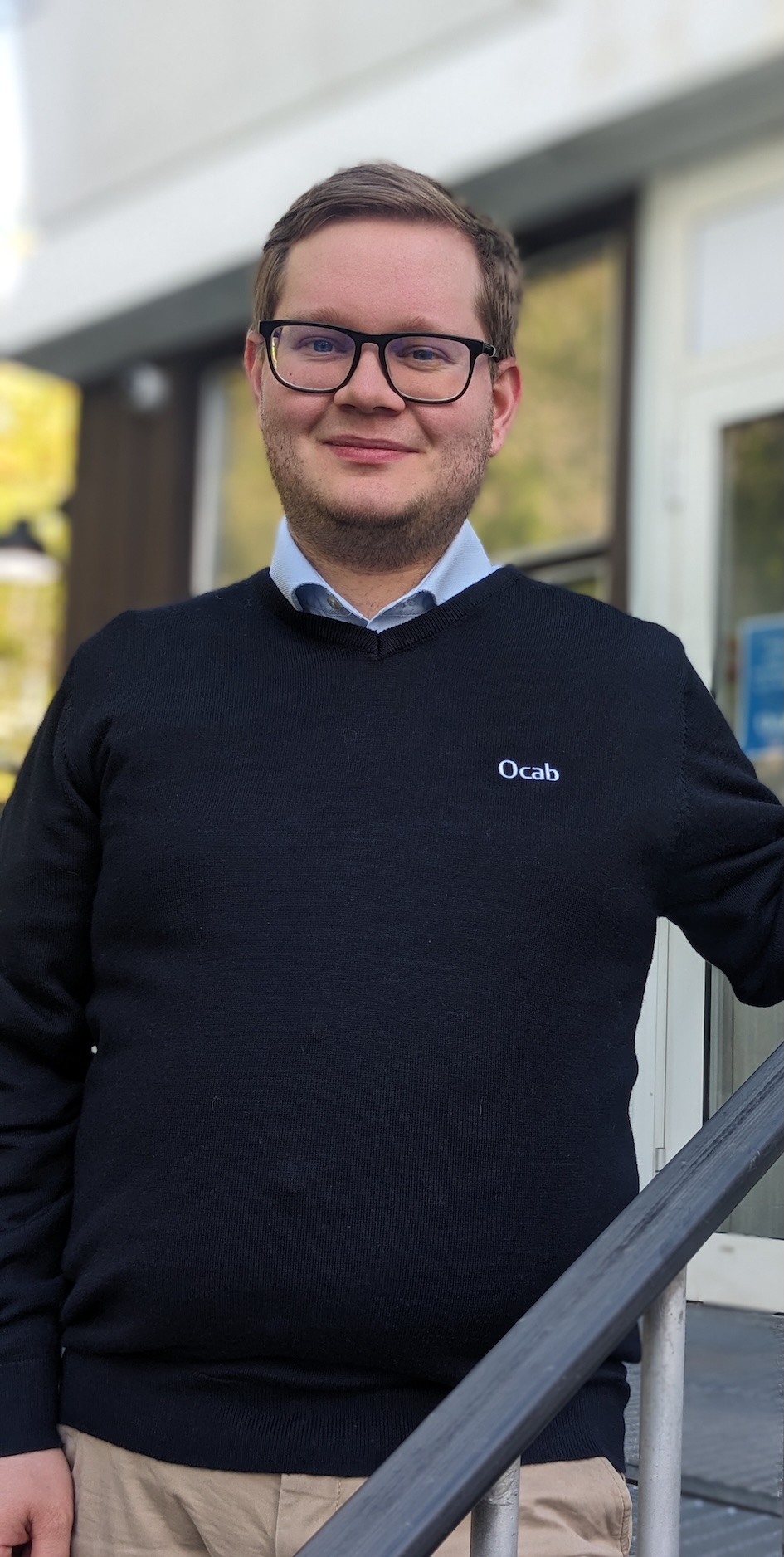 Mann stående i trapp med svart genser, og lener armen mot rekkverk.