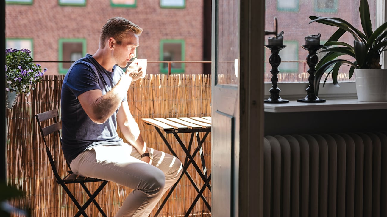 Mann på balkong som drikker kaffe i sola.