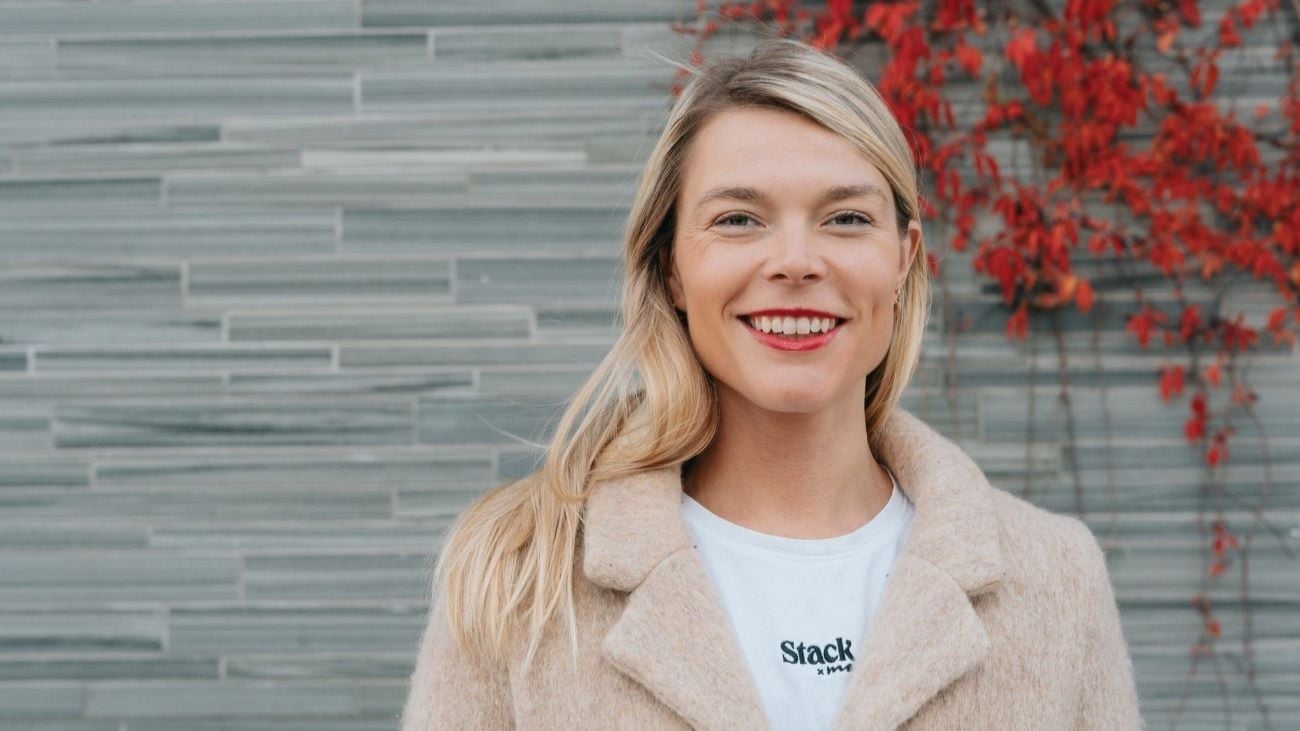 Kvinne som står foran en grå murvegg og smiler bredt til kamera.