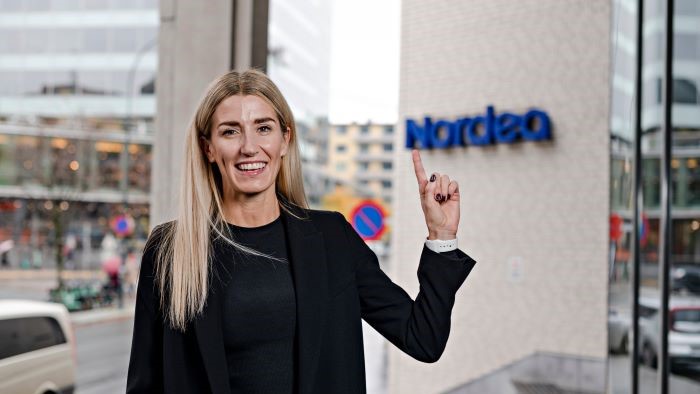 Kvinne som smiler og peker opp på et Nordea-skilt bak henne