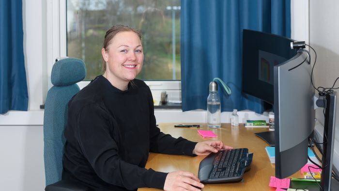 Smilende kvinne som sitter på et kontor med to PC-skjermer foran seg