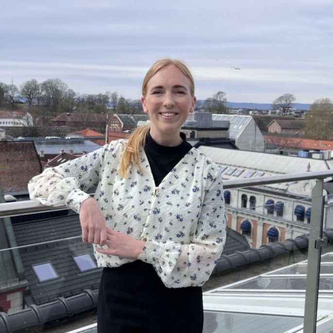 Ung kvinne som står på en takterrasse i Oslo og smiler bredt til kamera.