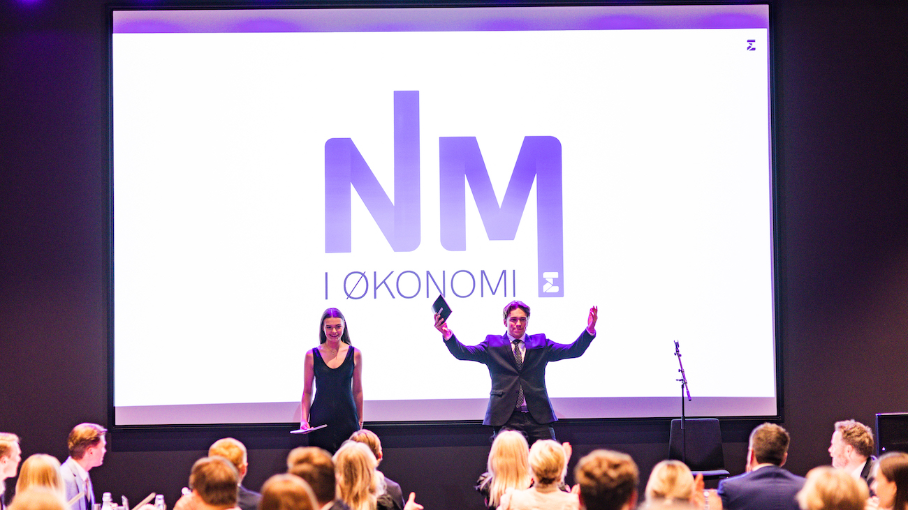 Konferansierene ønsker velkommen fra scenen med NM i økonomi logo i bakgrunnen.