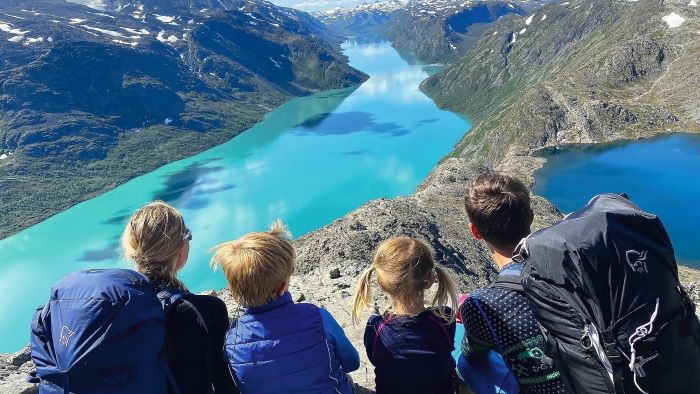 En familie på fire som sitter på en fjelltopp og ser ned mot fjorden.
