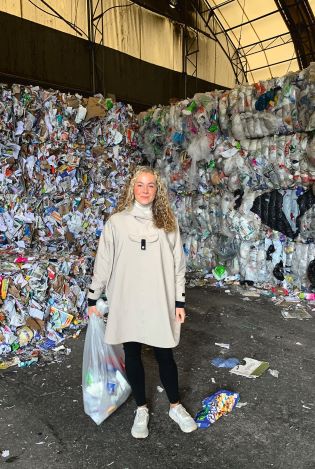 Ung kvinne som står foran en stor mengde søppel på en avfallsplass.