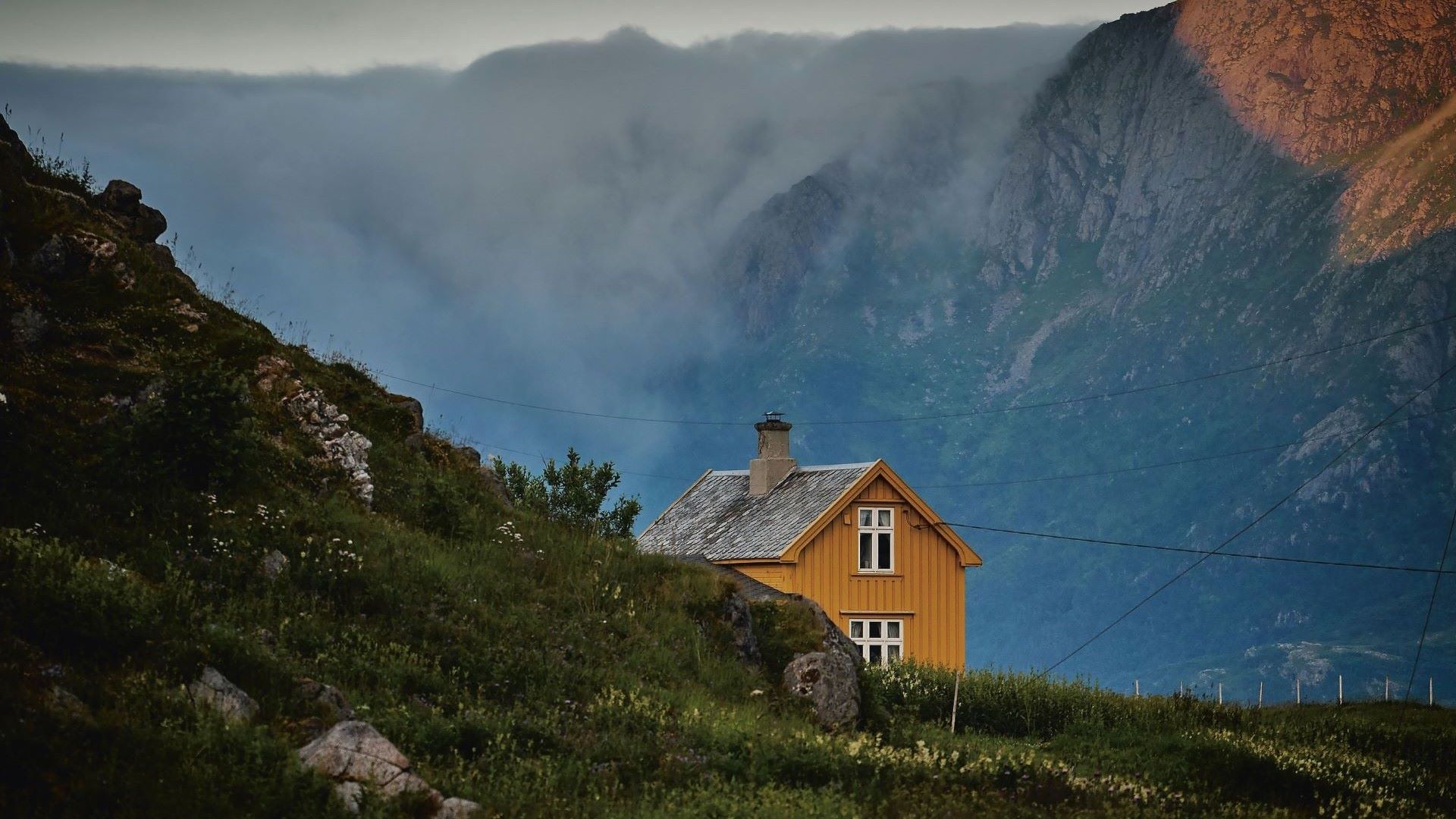 En gul hytte på et fjell med fjell i bakgrunnen.