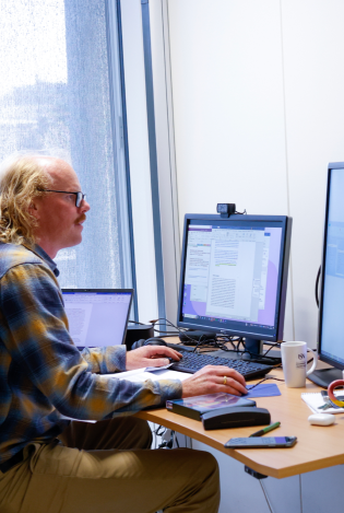 En mann som sitter på et kontor og jobber på to skjermer.