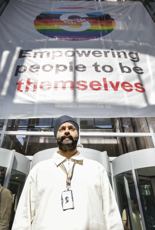 Froskeperspektiv av mann med turban som står foran et bygg. På bygget henger et banner med teksten " empowering people to be themselves".