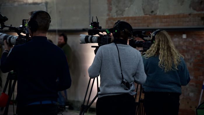 To kameramenn og en kamerakvinne som står og filmer et realityshow i et studio.
