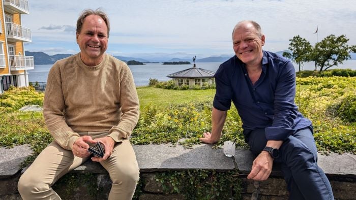 To menn som sitter på en steinvegg og smiler bredt til kamera.