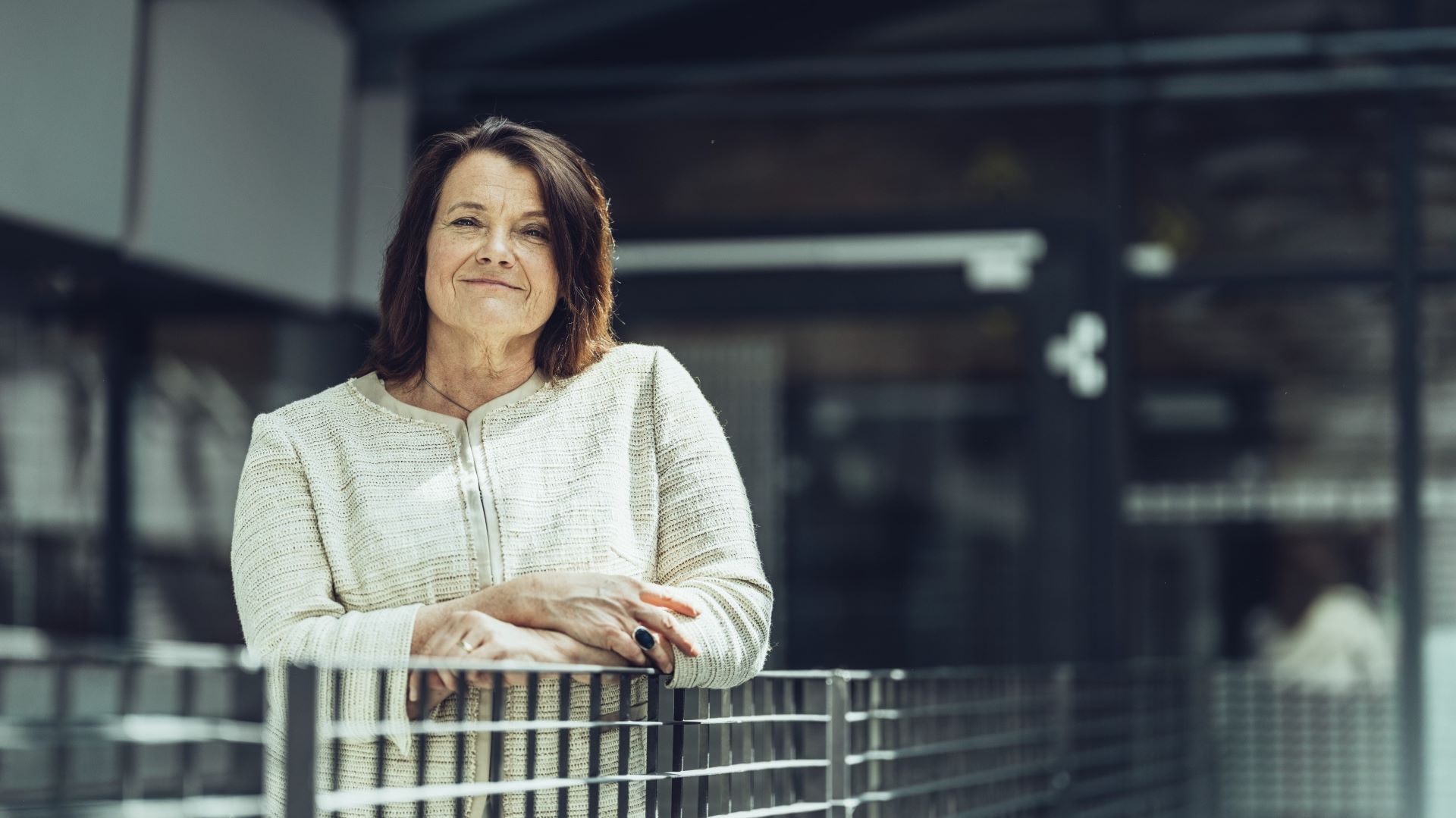 Kvinne som lener seg mot et gelender og smiler forsiktig til kamera.