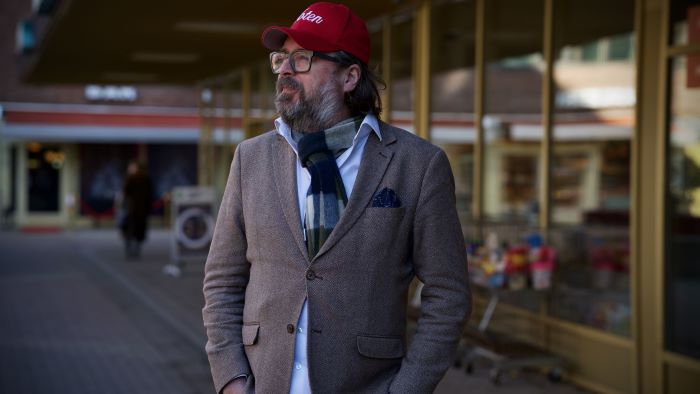 Mann som står med hendene i lommene og ser utover Tøyen torg mens han smiler forsiktig.