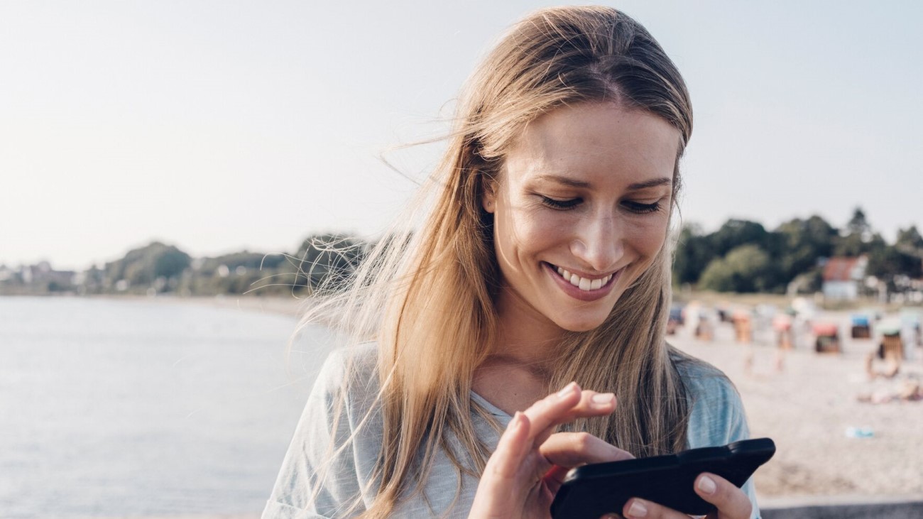 Smilende dame med mobil i hånden på en strand